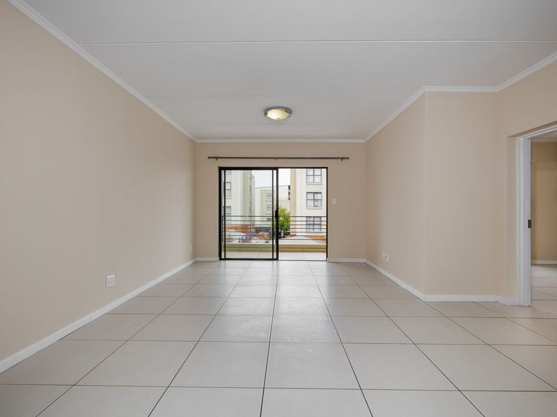 A spacious, empty open-plan living area featuring neutral walls, tiled flooring, and a sliding glass door leading to an outdoor balcony.