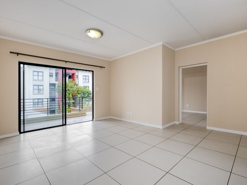A bright, empty living room featuring neutral tiled flooring, coving, and a large sliding glass door providing access to a private balcony.