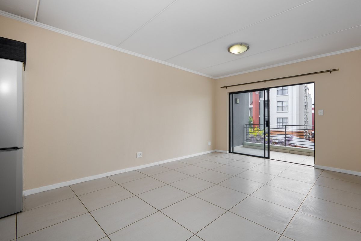 An empty, well-lit living area featuring neutral tiled flooring and a sliding glass door providing access to a private balcony.