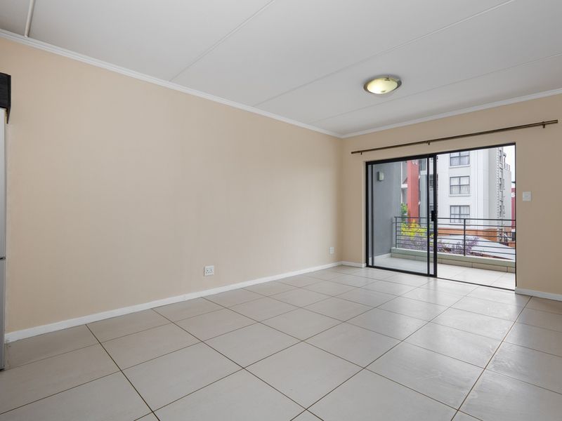 An empty, well-lit living area featuring neutral tiled flooring and a sliding glass door providing access to a private balcony.