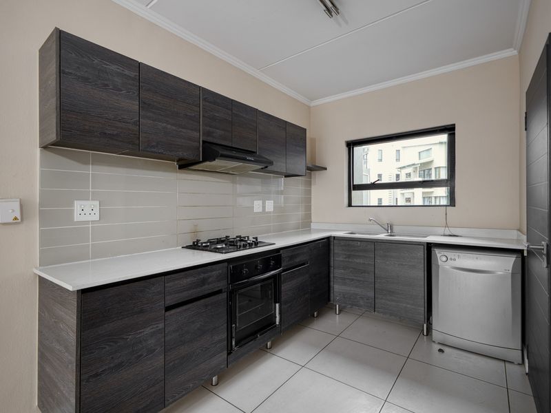 Modern kitchen featuring dark wood cabinetry, white stone countertops, built-in oven, gas hob, and tiled flooring in a clean, functional layout.