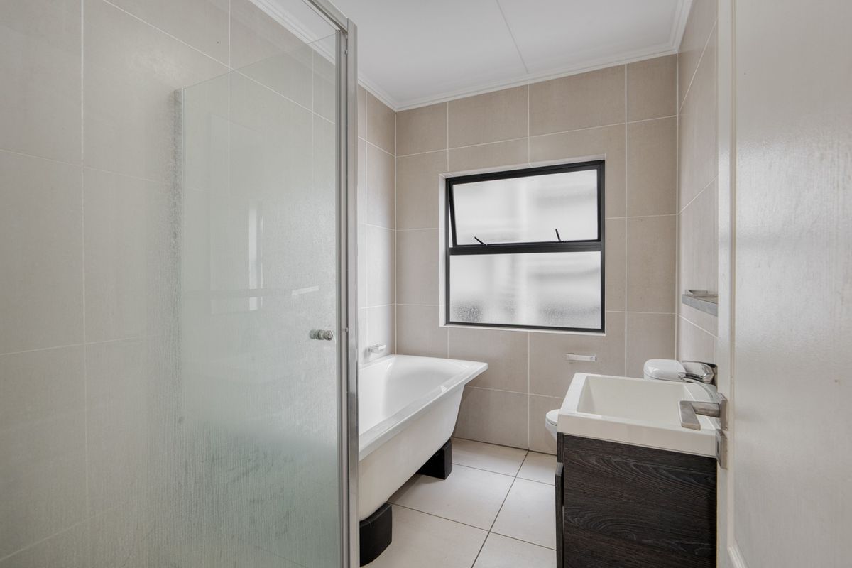 A clean, modern bathroom featuring a glass shower enclosure, a freestanding bathtub, and a vanity cabinet with a basin.