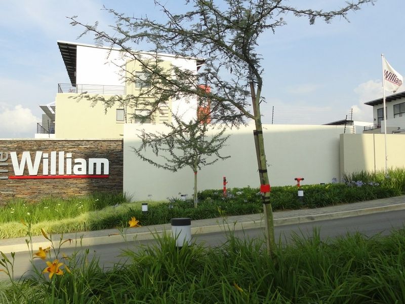 The entrance facade of The William apartment complex, featuring modern stone cladding, perimeter walling, and well-maintained landscaped grounds.