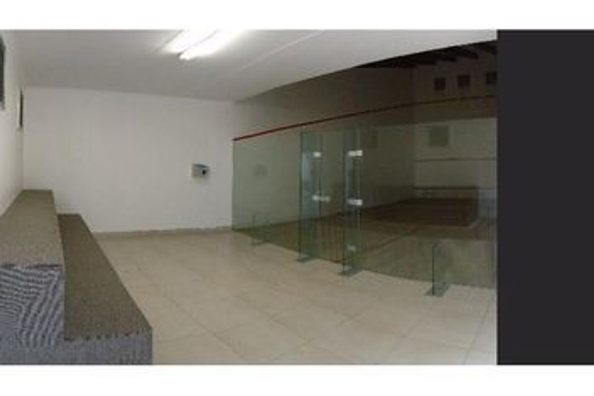 A dedicated squash court facility featuring a glass partition, tiled flooring, and functional overhead lighting.
