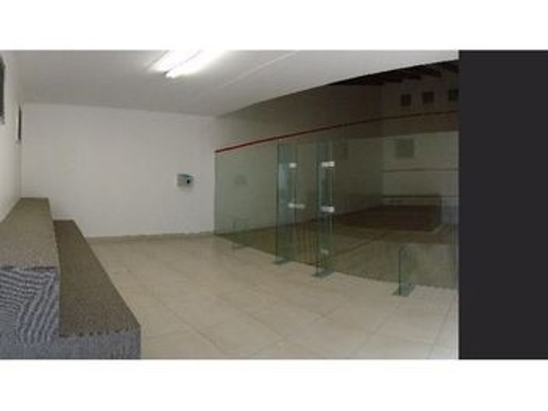 A dedicated squash court facility featuring a glass partition, tiled flooring, and functional overhead lighting.