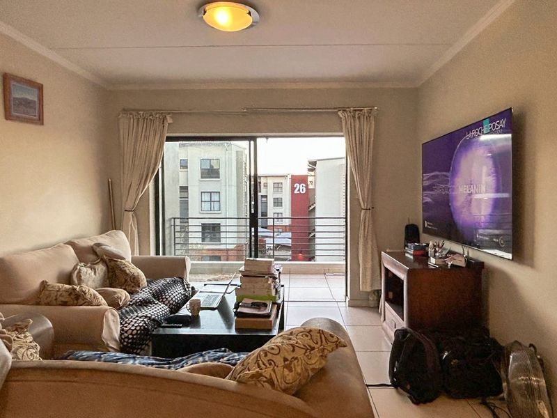 A living room featuring tiled flooring and a sliding glass door that opens onto a balcony, providing natural light and an urban view.