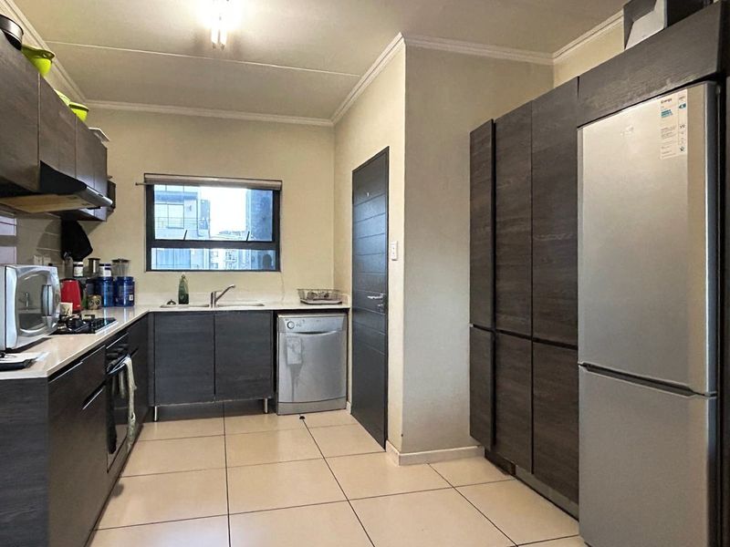 A functional kitchen featuring dark wood-look cabinetry, light tiled flooring, integrated appliances, and a window providing natural light.