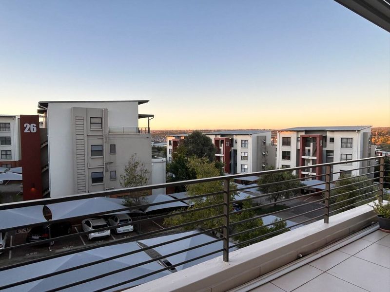 A spacious balcony featuring tiled flooring and a secure metal balustrade, offering elevated views over the apartment complex and parking area.