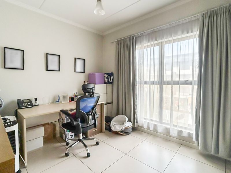 A functional office space featuring tiled flooring and a large window with curtain tracks, providing natural light.