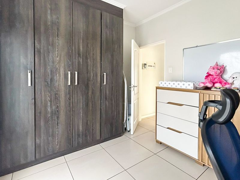 A bedroom featuring dark wood-grain built-in cupboards, neutral tiled flooring, and a clean, well-maintained interior finish.