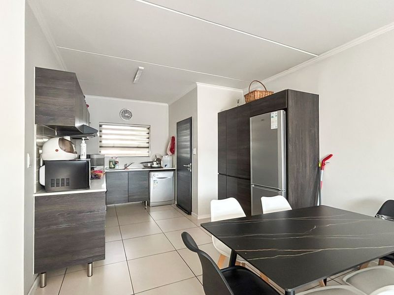 Open-plan kitchen and dining area featuring modern dark wood cabinetry, tiled flooring, and functional built-in storage solutions.