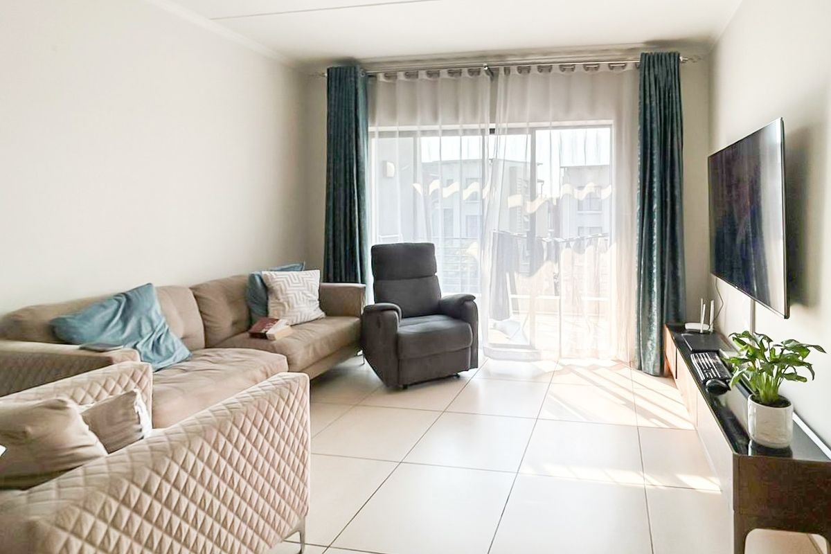 A bright living room featuring large format floor tiles and a sliding glass door providing access to an outdoor balcony area.