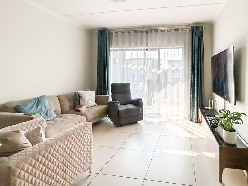 A bright living room featuring large format floor tiles and a sliding glass door providing access to an outdoor balcony area.
