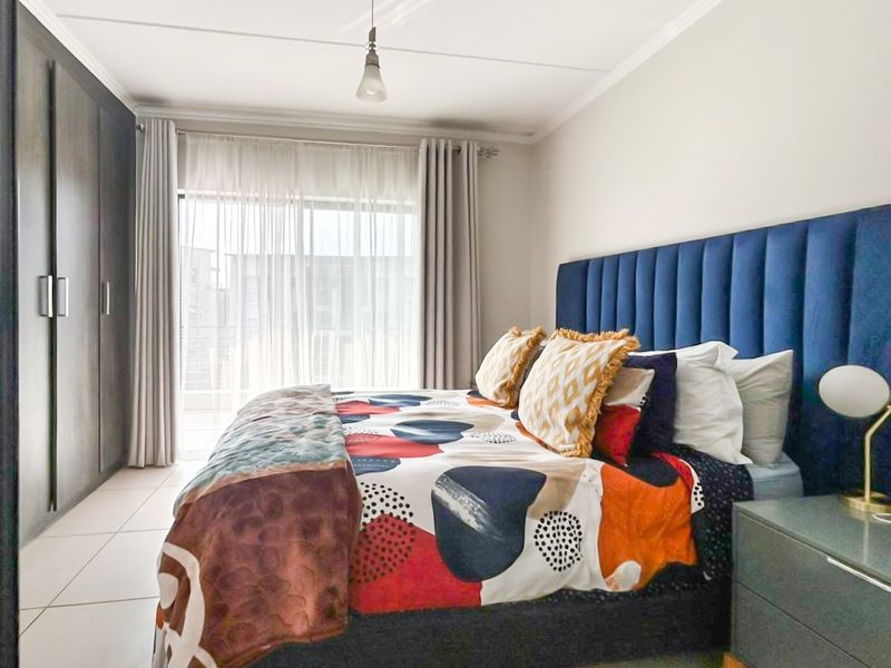 A well-maintained bedroom featuring built-in cupboards, tiled flooring, and a sliding glass door providing access to an outdoor area.