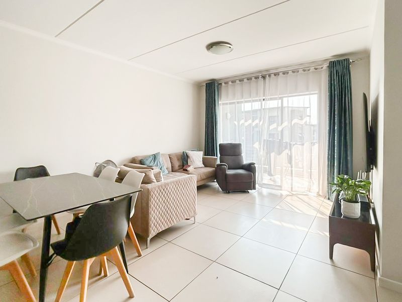 Bright open-plan living and dining area featuring large format floor tiles and a sliding glass door providing access to the balcony.