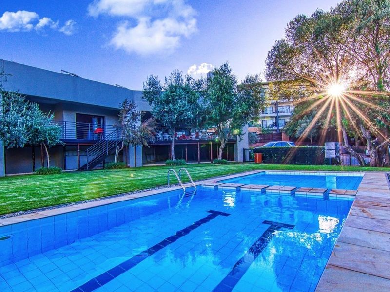 A well-maintained communal swimming pool area featuring a landscaped garden, paved pool surround, and access to the apartment building's balcony.