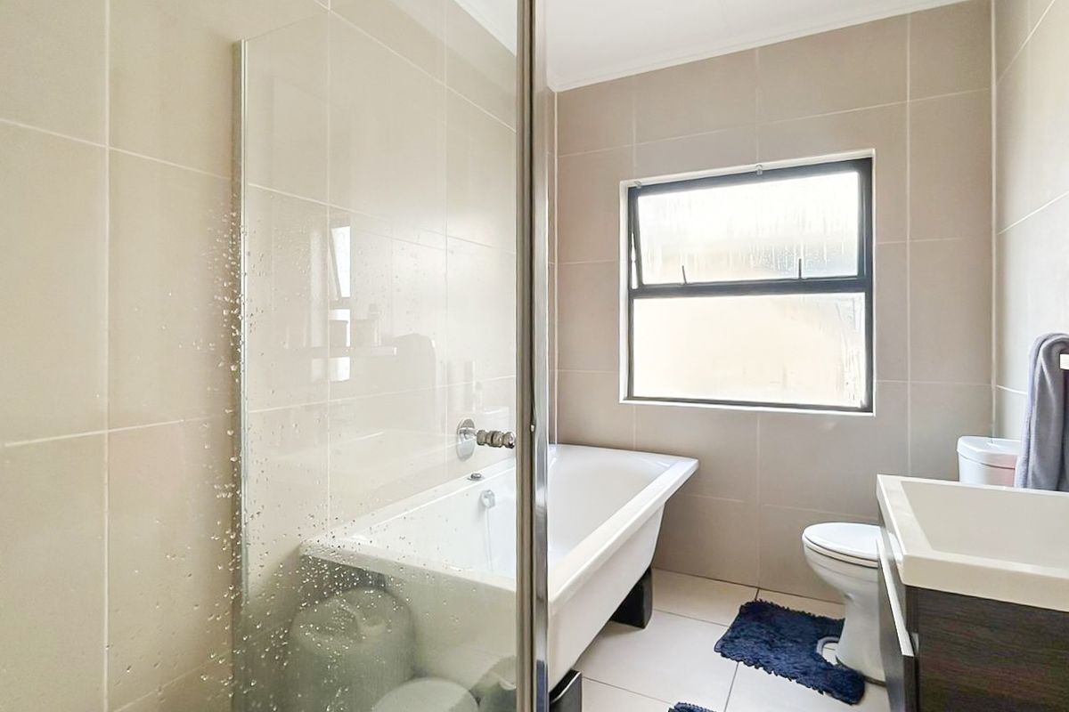 A modern bathroom featuring a bathtub, glass shower screen, toilet, and a vanity cabinet with a basin, finished with neutral wall and floor tiles.