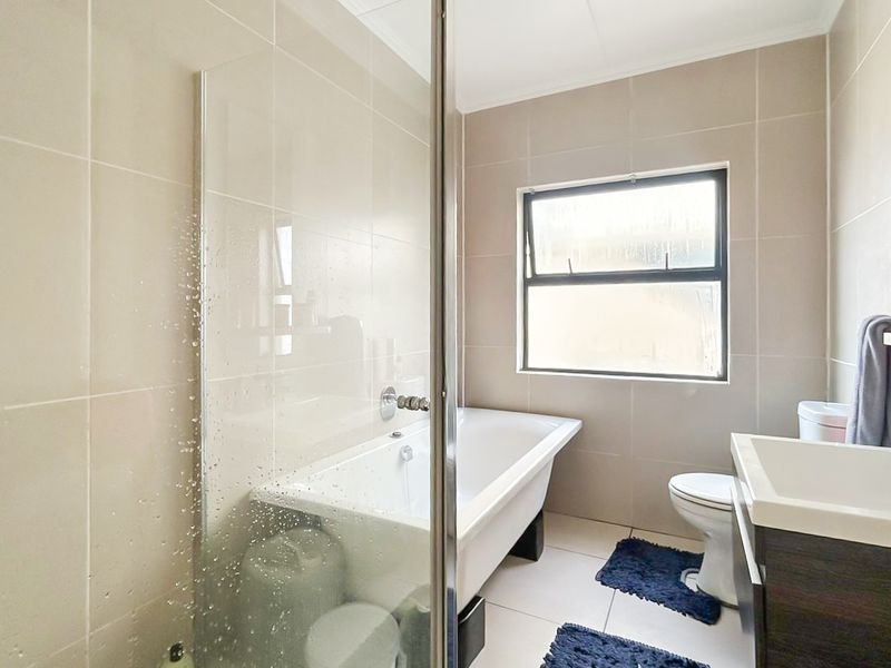 A modern bathroom featuring a bathtub, glass shower screen, toilet, and a vanity cabinet with a basin, finished with neutral wall and floor tiles.