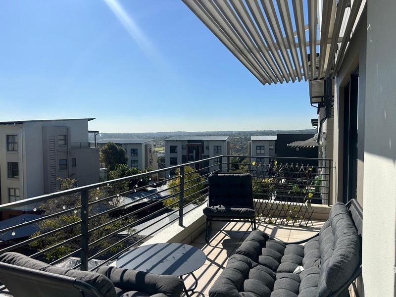 A spacious balcony featuring a slatted overhead pergola, metal balustrade, and tiled flooring, offering elevated views of the surrounding neighborhood.