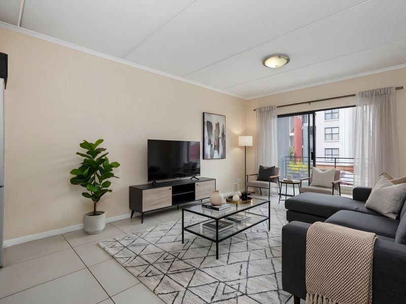 A bright and well-maintained living room featuring tiled flooring and a large sliding glass door that provides access to a balcony.