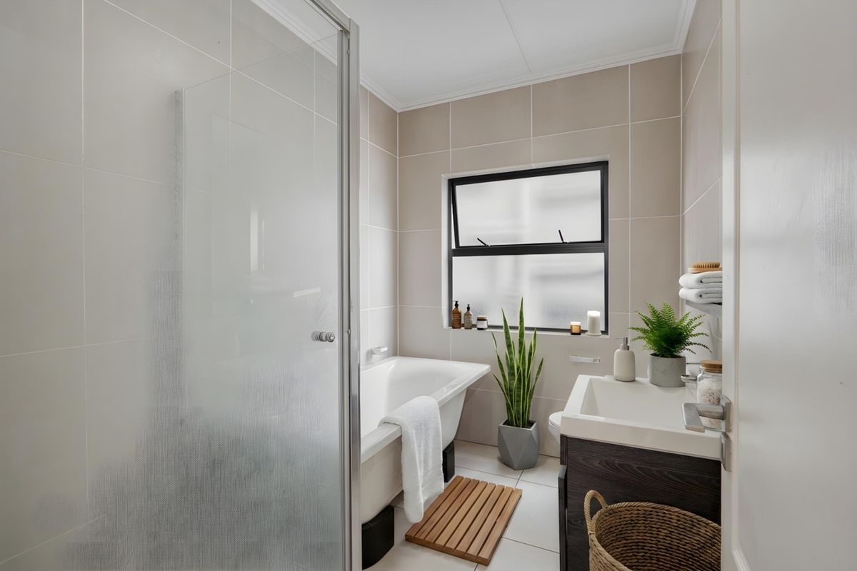 A modern, well-maintained bathroom featuring a shower enclosure, a bathtub, and a vanity cabinet with a basin, finished with neutral wall and floor tiles.