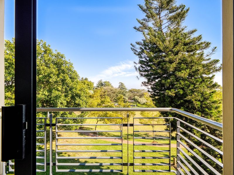 A balcony featuring a modern stainless steel railing with clear views overlooking a lush green park and mature trees.