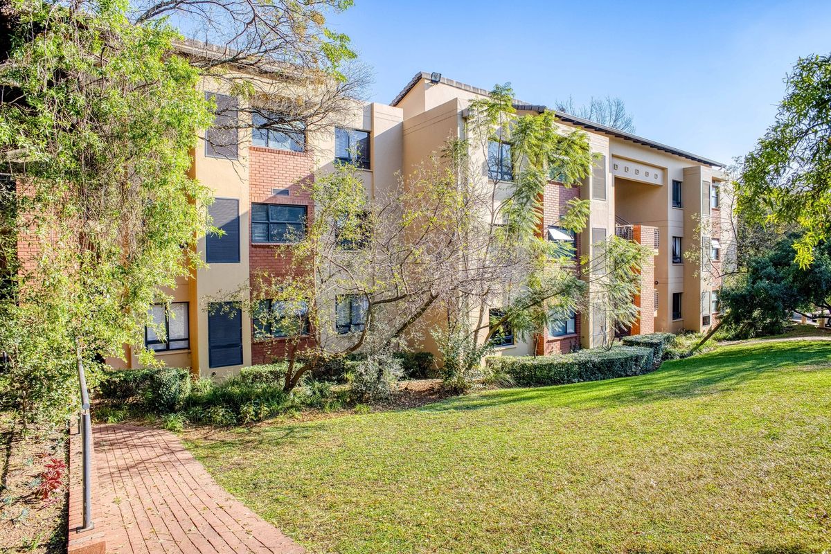 A view of the rear facade of a multi-story residential building featuring brick and plaster finishes, set within a well-maintained garden area.