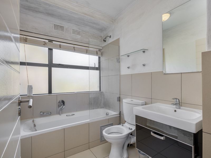 A functional bathroom featuring a bathtub with shower attachment, a modern vanity unit, and neutral wall tiling.