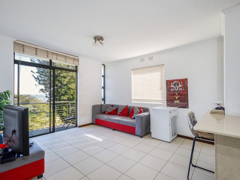 Open plan living area featuring tiled flooring, a built-in breakfast bar, and large sliding glass doors leading to an outdoor balcony with scenic views.