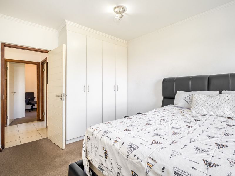 A well-maintained bedroom featuring neutral carpeted flooring, built-in cupboards, and direct access to an adjacent hallway.