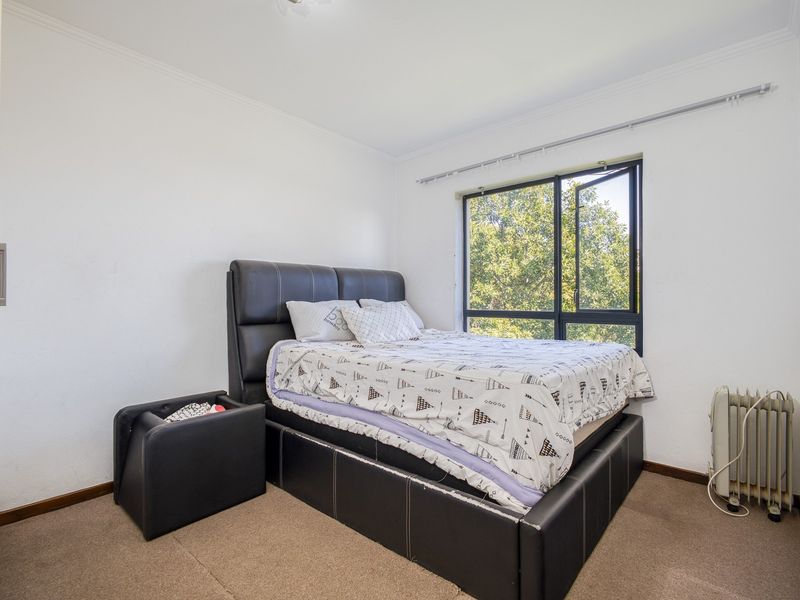 A functional bedroom featuring carpeted flooring, a built-in cupboard, and a large aluminium-framed window providing natural light and garden views.