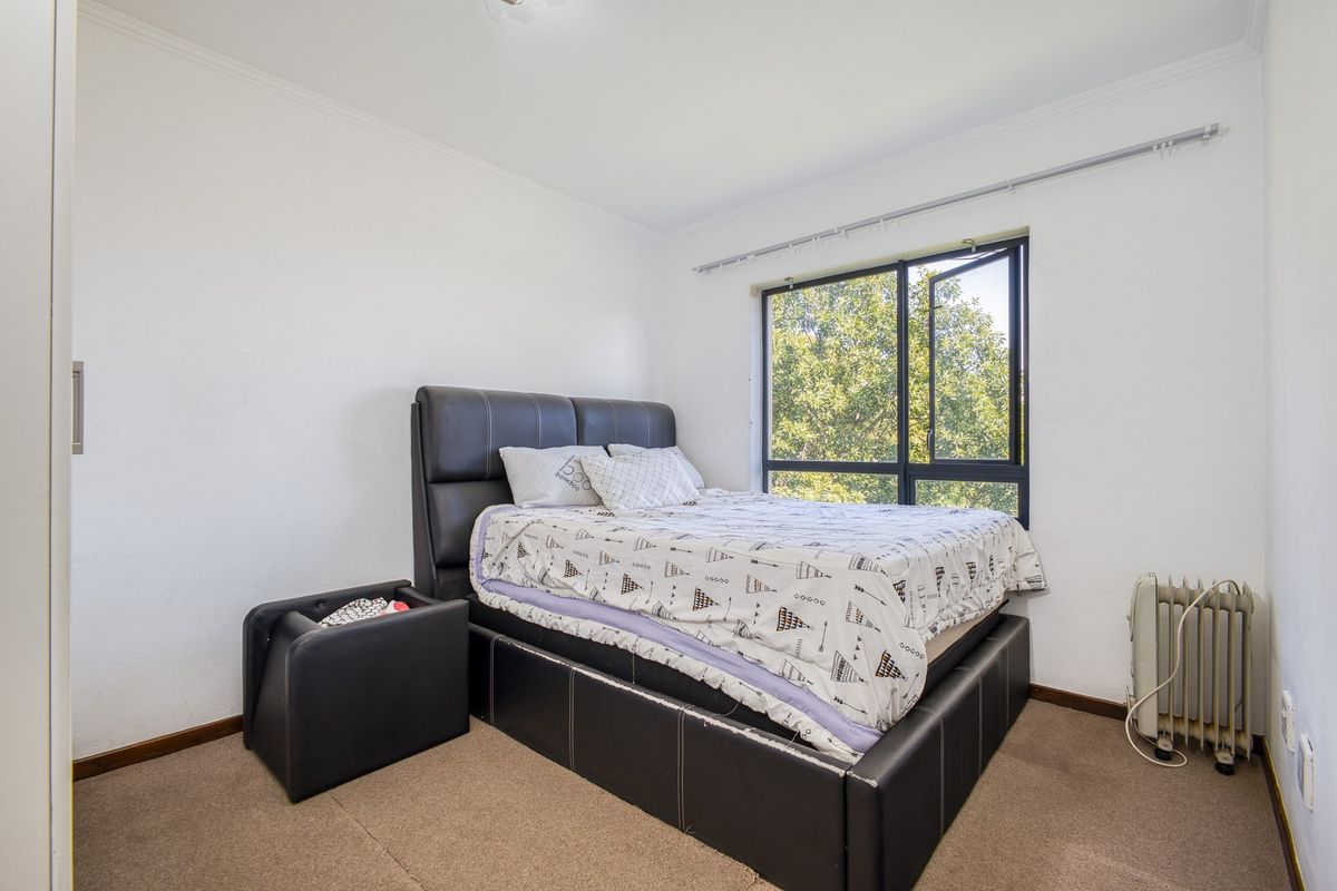 A functional bedroom featuring carpeted flooring, a built-in cupboard, and a large aluminium-framed window providing natural light and garden views.