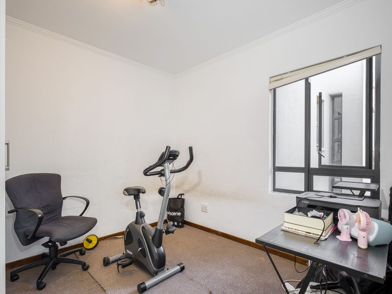 A small office or study room featuring carpet flooring and an aluminium window frame, currently used as a home gym and workspace.