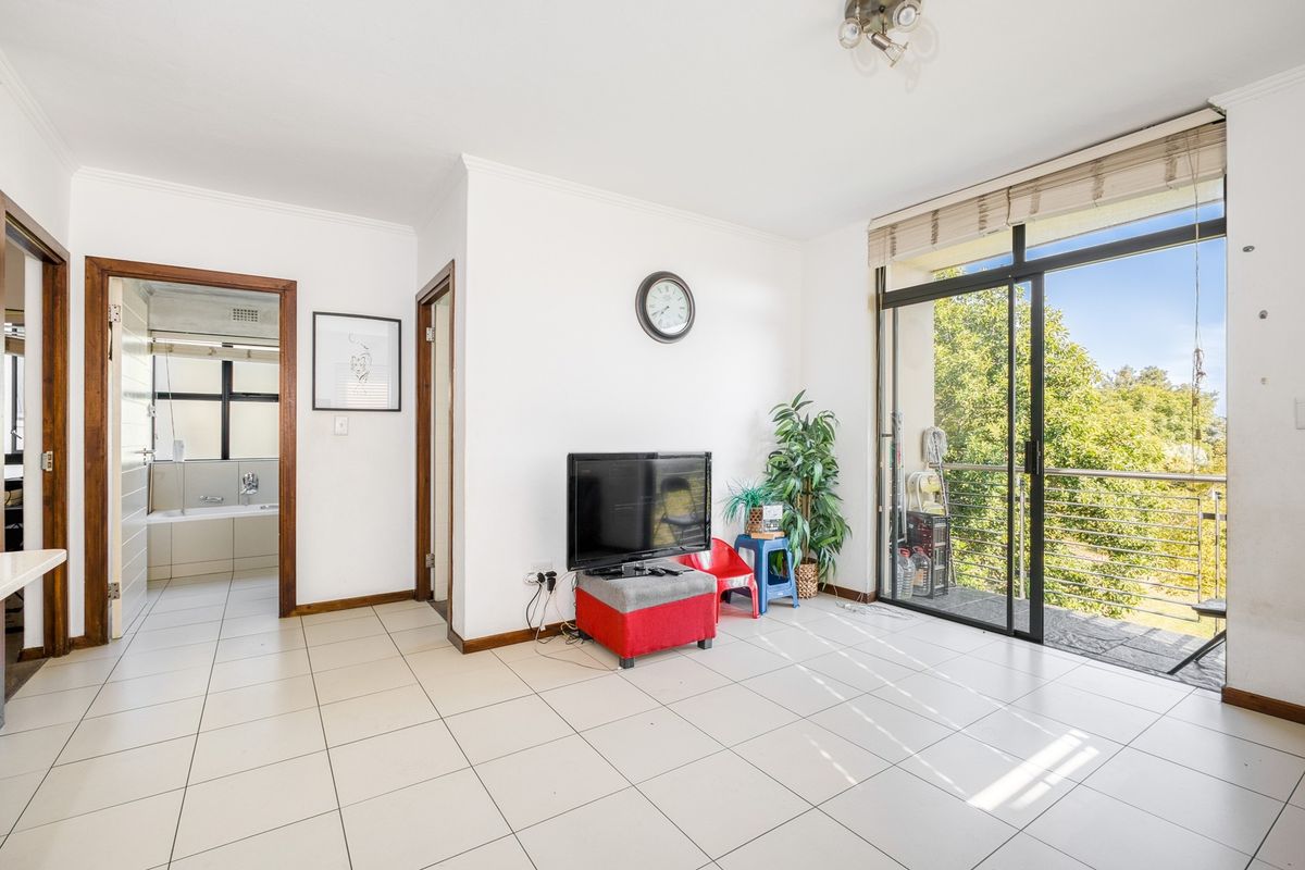 A bright living room featuring tiled flooring, coving, and large sliding glass doors providing access to an outdoor balcony area.
