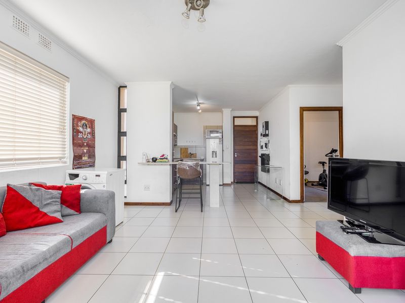 Open-plan living area featuring tiled flooring, a breakfast bar, and an integrated kitchen space with neutral finishes.