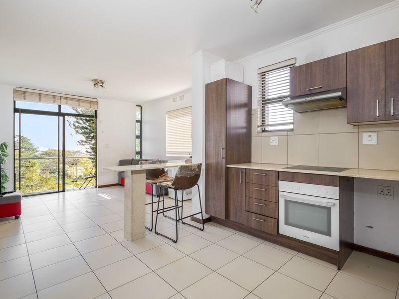 Open-plan kitchen and living area featuring dark wood cabinetry, stone countertops, tiled floors, and large sliding doors leading to an outdoor balcony.