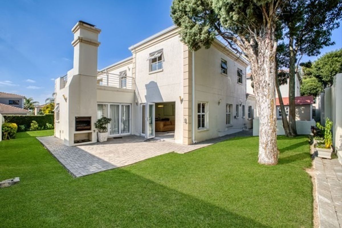 Rear view of the property featuring a paved patio area with a built-in braai, balcony, and well-maintained garden space.
