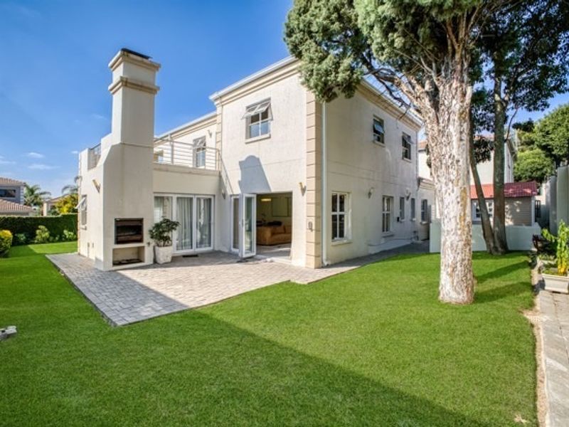 Rear view of the property featuring a paved patio area with a built-in braai, balcony, and well-maintained garden space.
