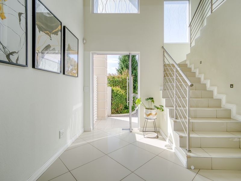 Bright and spacious double-volume entrance hall featuring tiled flooring, a modern staircase with stainless steel railings, and large windows allowing ample natural light.