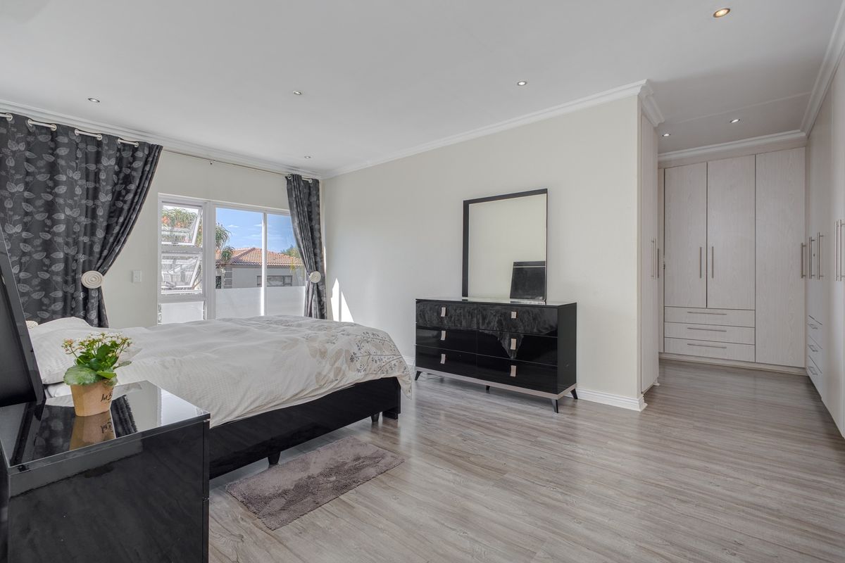 Spacious bedroom featuring light laminate flooring, recessed downlighting, and extensive built-in cabinetry, with direct access to an outdoor area via sliding glass doors.