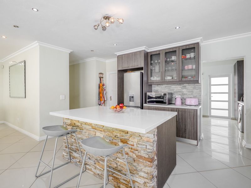 Modern kitchen featuring a stone-clad island with quartz countertop, sleek dark wood cabinetry, glass-fronted display units, and polished porcelain floor tiles.