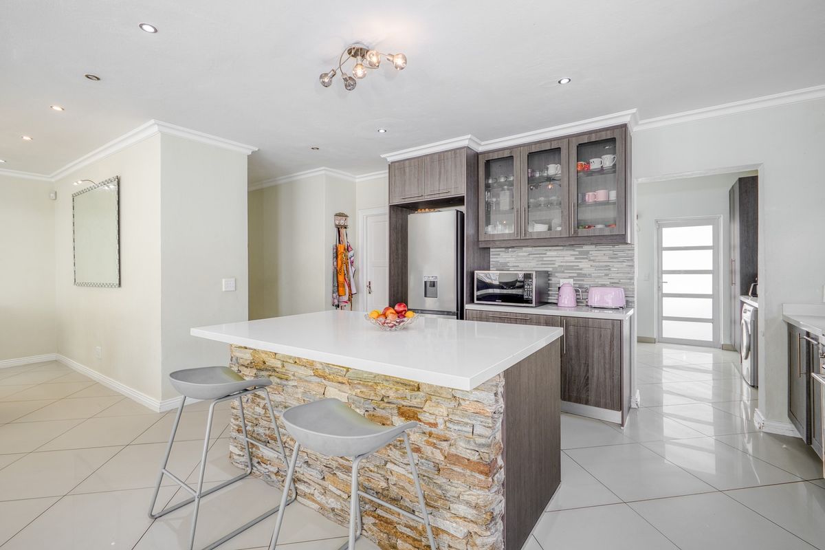 Modern kitchen featuring a stone-clad island with quartz countertop, sleek dark wood cabinetry, glass-fronted display units, and polished porcelain floor tiles.