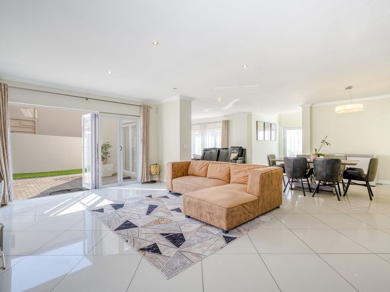 Spacious open-plan living and dining area featuring polished porcelain tiles, recessed lighting, and seamless access to the outdoor patio through bi-fold glass doors.