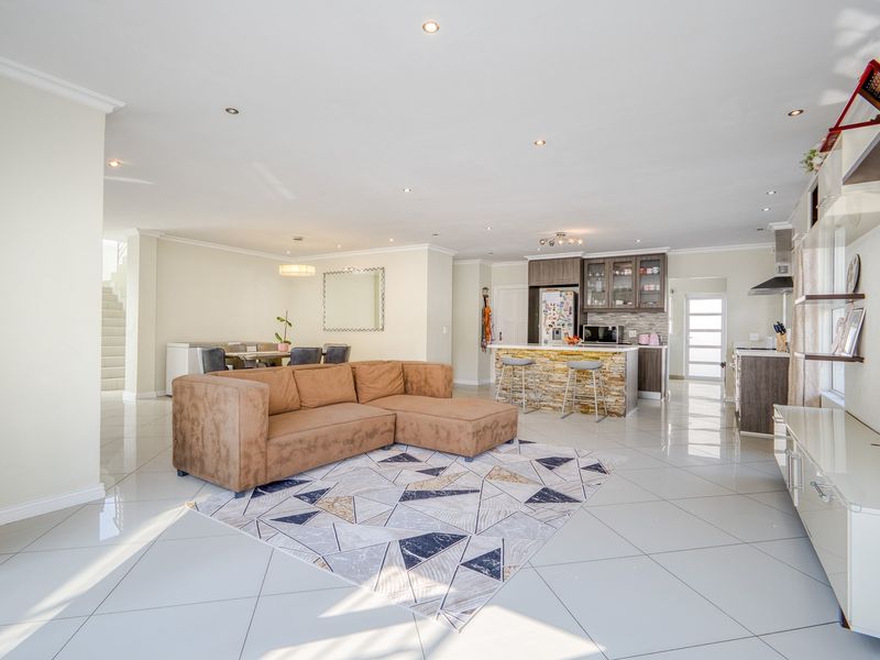 Spacious open-plan living area featuring polished porcelain tiles, recessed lighting, and a modern kitchen with a stone-clad breakfast island.