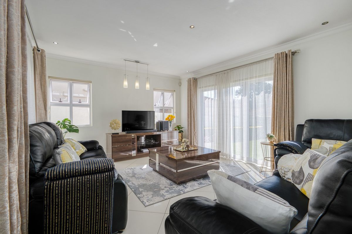A bright and well-maintained living room featuring tiled flooring, recessed downlights, and large sliding glass doors that provide access to the outdoor area.