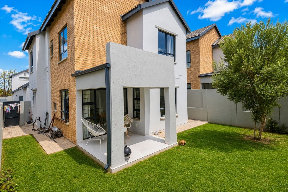 Rear view of the townhouse featuring a covered patio with tiled flooring, brick and plastered exterior walls, and a private garden area.