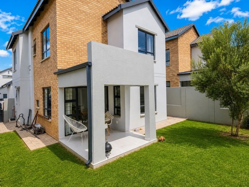 Rear view of the townhouse featuring a covered patio with tiled flooring, brick and plastered exterior walls, and a private garden area.