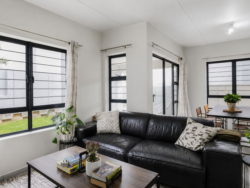 Bright open-plan living and dining area featuring modern black-framed windows with security bars and direct access to the outdoor space.