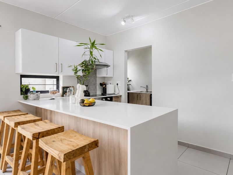 Modern kitchen featuring white cabinetry, a breakfast bar with stone countertop, and a tiled backsplash, with an adjacent scullery area.