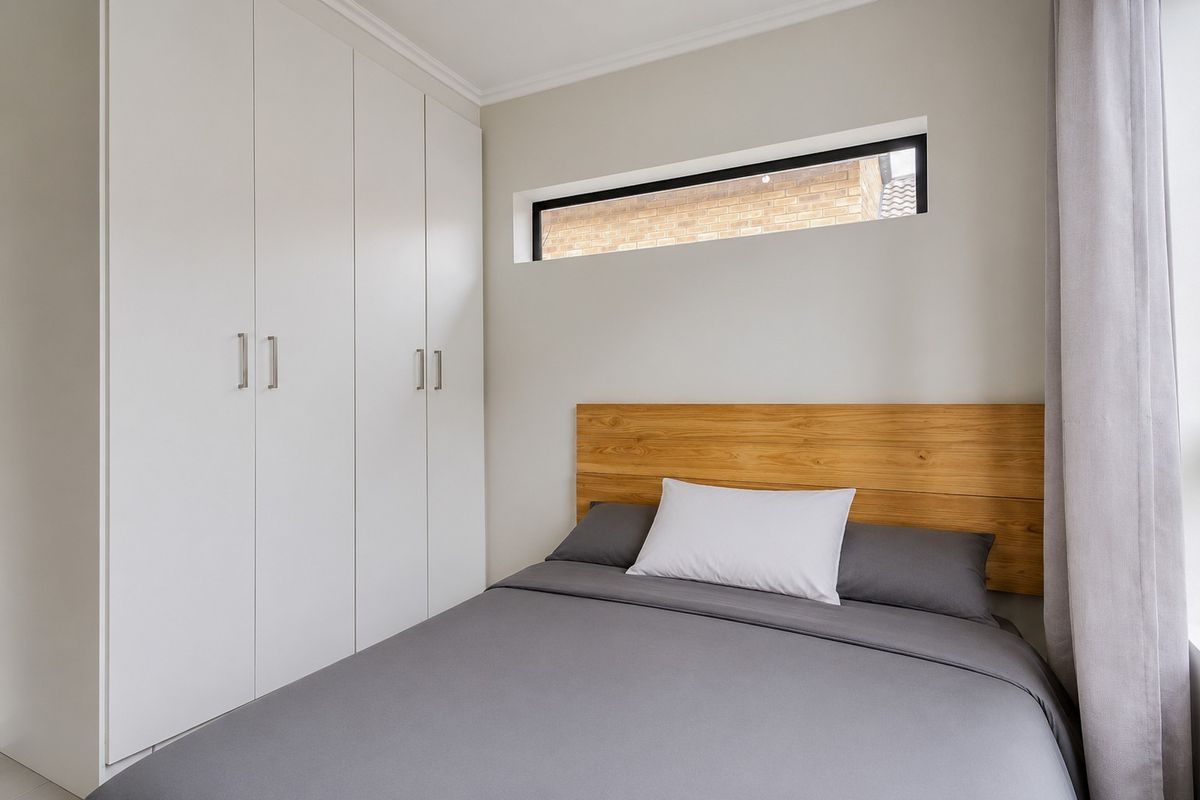 A modern bedroom featuring a built-in wardrobe, a sleek clerestory window, and neutral finishes, creating a clean and functional living space.